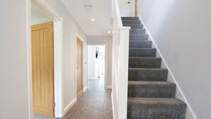 A staircase with carpeted steps leading to a landing, adjacent to a wooden door and a hallway with a light-colored floor. - Field View 5-bed House - Free Parking (Burton on Trent)