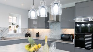 A modern kitchen with a marble countertop, a bottle of champagne, and a fruit bowl. - Field View 5-bed House - Free Parking (Burton on Trent)