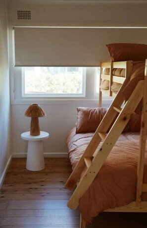 A small, cozy room with a bunk bed, a small table with a lamp, and a window with a view of the outdoors. - Sunset Beach House (Soldiers Point)