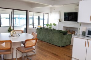 A modern living room with a white fireplace, a green sofa, and a dining area with a round table and chairs. - Sunset Beach House (Soldiers Point)
