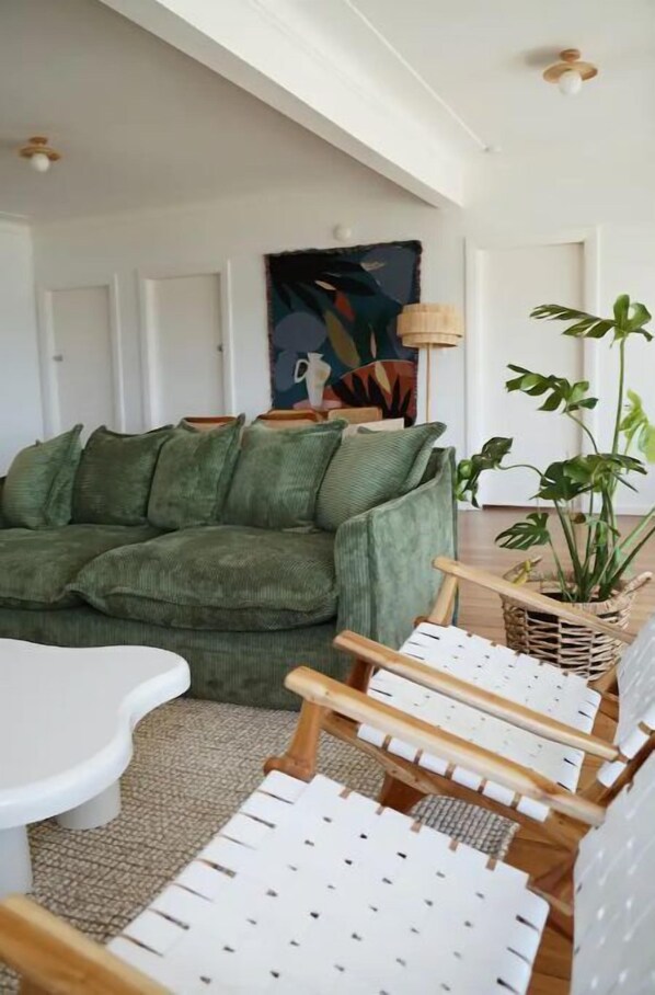 A living room with a green sofa, white armchairs, a coffee table, and a large plant. - Sunset Beach House (Soldiers Point)