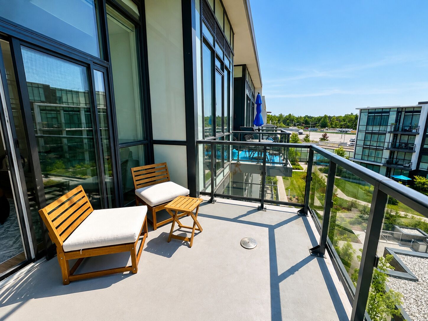 A balcony with two wooden chairs and a small table, overlooking a swimming pool and a parking area.