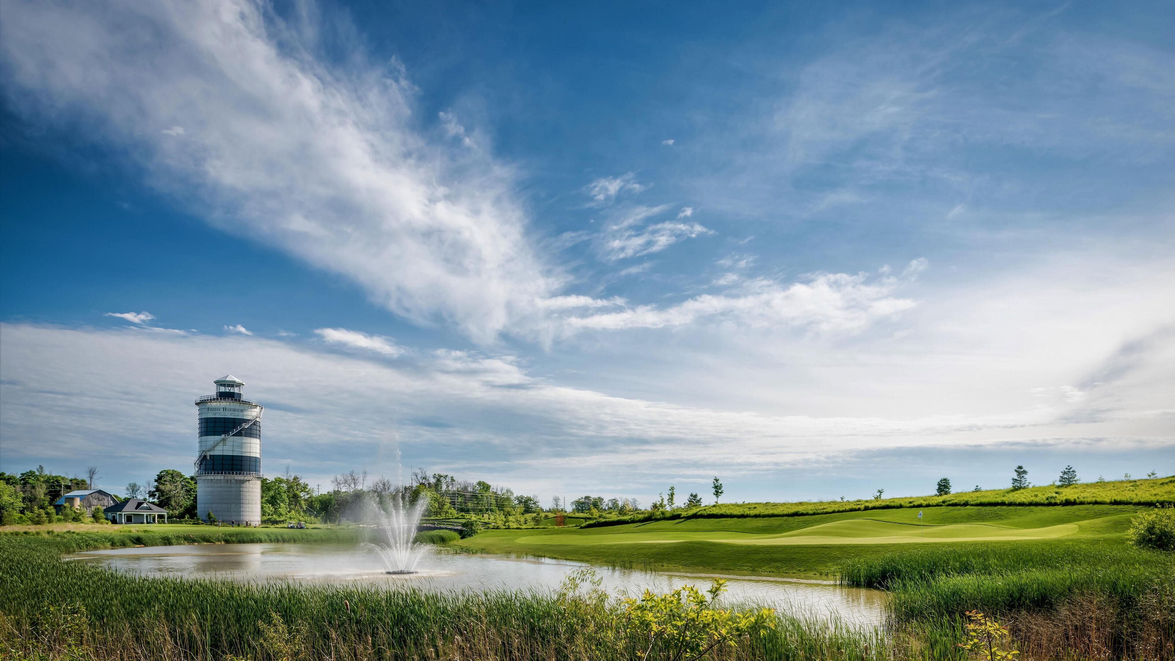 A golf course with a water fountain, a water tower, and a clear sky.