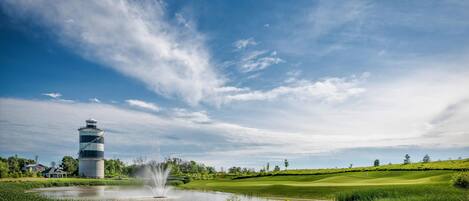 A golf course with a water fountain, a water tower, and a clear sky.