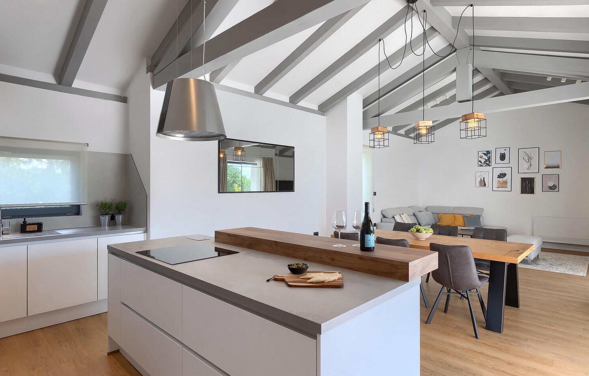 A modern kitchen with a central island, a dining area with a wooden table, and a living space with a sofa and artwork on the walls.