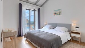 A bedroom with a large bed, a nightstand, a bedside table, and a view of a swimming pool through a sliding glass door.