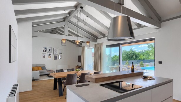 A modern kitchen with a large island, dining area with a wooden table, and a view of a swimming pool.