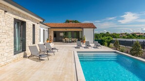 A modern poolside area with a clear blue pool, lounge chairs, and a dining area with a table and chairs.
