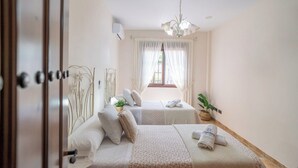 A hotel room with two beds, a chandelier, a window with curtains, and a plant. - Villa Almijara Cómpeta by Ruralidays (Málaga)