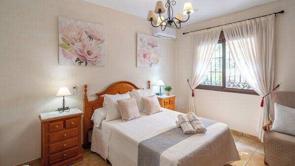 A bedroom with a wooden bed, bedside tables, a chandelier, and floral artwork on the walls.