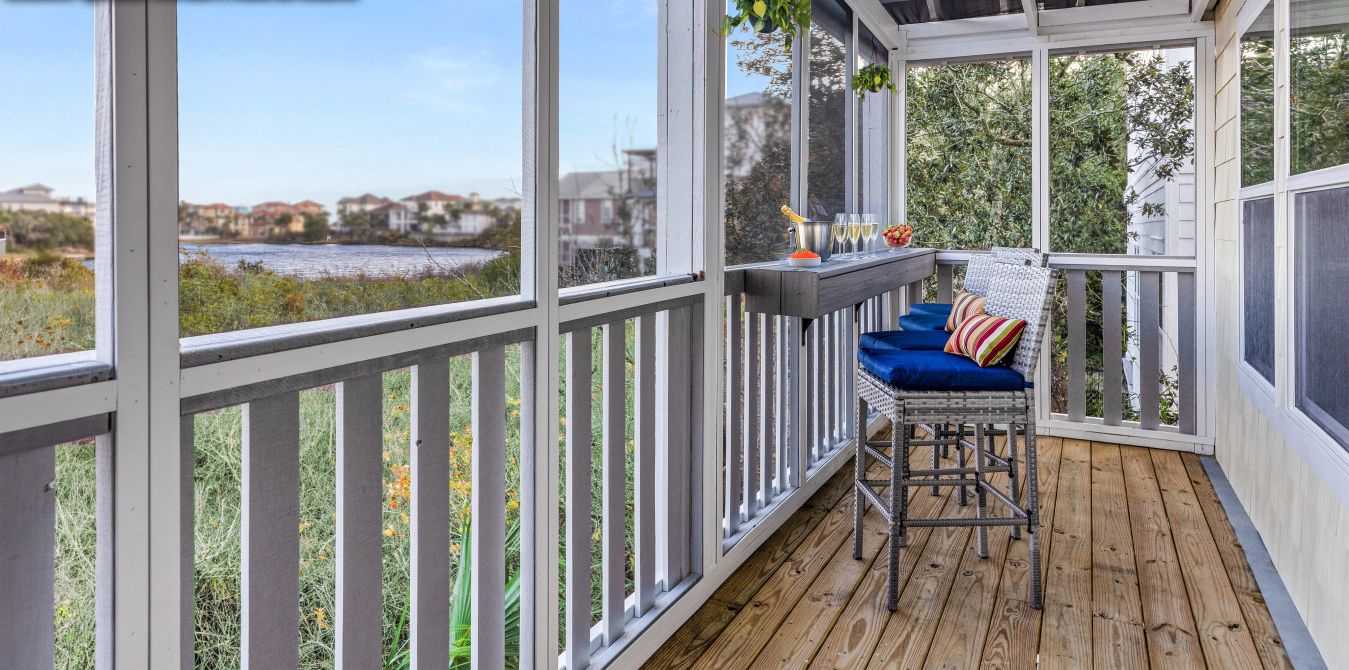 Un espace extérieur abrité doté d’une terrasse en bois, d’un coin salon avec des coussins bleus, et de plantes suspendues.