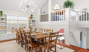 A dining area with a wooden table set for six, surrounded by chairs. A high ceiling fan is visible, and there are shelves with decorative items and plants. - 3min walk to private beach access, saltwater spa & pool (Destin)