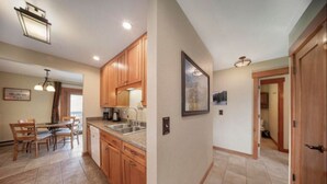 A modern kitchen with wooden cabinets, a dining area with a table and chairs, and a hallway leading to a bathroom. - Riverside Ground-Level Condo in Funky Fraser. (Fraser)