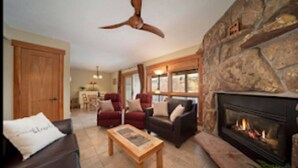 A living room with a stone fireplace, a ceiling fan, and a large wooden door. - Riverside Ground-Level Condo in Funky Fraser. (Fraser)