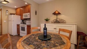 A kitchen with wooden cabinets, a microwave, a stove, and a dining table with chairs. - Riverside Ground-Level Condo in Funky Fraser. (Fraser)