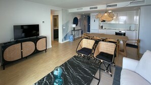 Una sala de estar moderna con televisor de pantalla plana, sillas de mimbre, una mesa de centro de mármol y un comedor con mesa y sillas de madera.