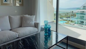 Una sala de estar moderna con un sofá, una mesa de centro de vidrio y vistas a una piscina y edificios.