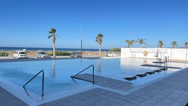 Una piscina con vista despejada al océano, palmeras y un estacionamiento con automóviles.