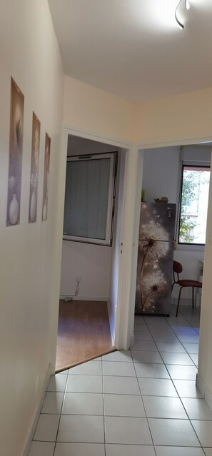 A hallway with a tiled floor, a door leading to a room with a window, and a refrigerator with a dandelion decoration. - Apartment 'Oasis T3' with Shared Terrace, Private Garden and Wi-Fi (Villeurbanne)