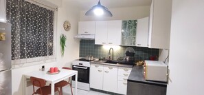 A compact kitchen with white cabinets, a black countertop, a built-in oven, a coffee machine, and a hanging plant.