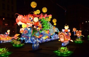 A large, illuminated dragon float with figures on it, likely part of a festival or parade.