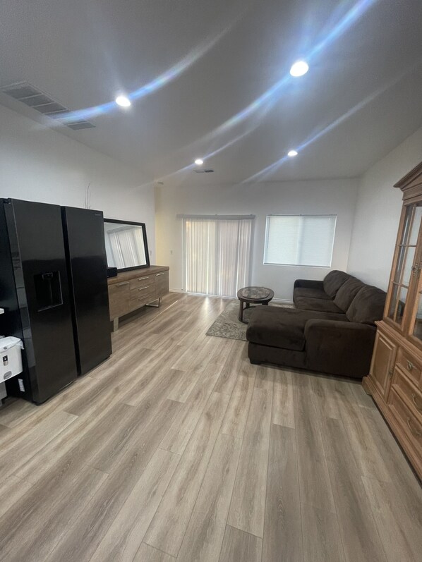 Een ruime woonkamer met een moderne keuken, een bruine leren bank en een houten kast.