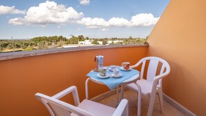 Un balcón con una mesa para dos, una cafetera y tazas.