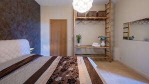 Un dormitorio con cama, lámpara colgante, estante de madera con cajas, una puerta y un espejo en la pared.