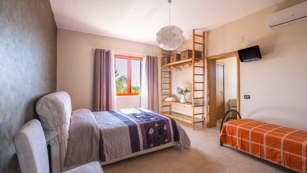 Ein Schlafzimmer mit Bett, Sofa, einer Leiter, einem Fernseher und einem Fenster mit Vorhängen.