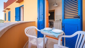 A balcony with two white plastic chairs, a table with plates and glasses, and blue shutters on the building.
