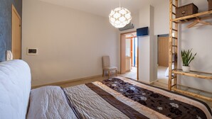 A bedroom with a bed, a hanging light fixture, a chair, a wooden ladder, and a potted plant.