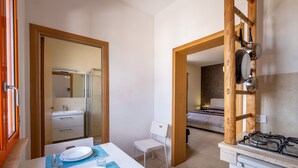 A compact kitchen with a gas stove, a dining table set with plates and cutlery, a white chair, and a small sink. - Apartment "Terra E Colori Bilo 1" with Wi-Fi & Air Conditioning (Gallipoli)