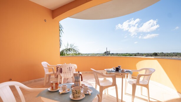 A balcony with a table set for two, white plastic chairs, and a view of the landscape. - Apartment "Terra E Colori Bilo 1" with Wi-Fi & Air Conditioning (Gallipoli)