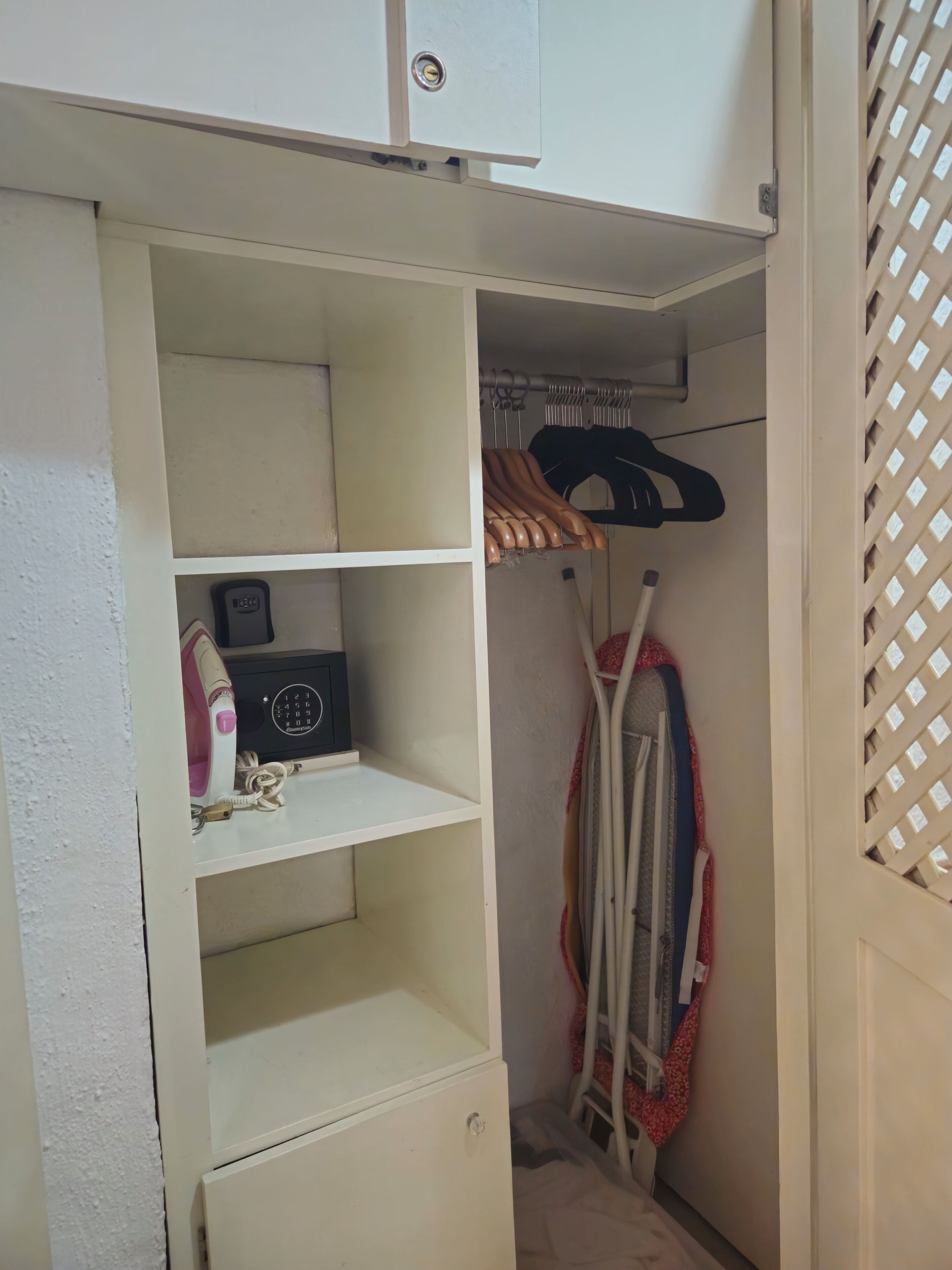 Um guarda-roupa branco com prateleiras, cabideiro e um pequeno ferro de passar.