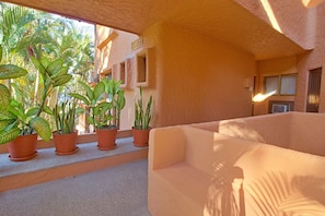 Un espace extérieur ensoleillé, aménagé avec des jardinières en terre cuite et un banc beige doté de coussins.