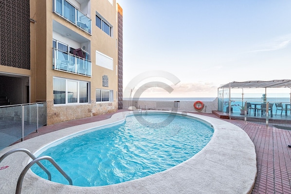 Une piscine dotée d’une balustrade en verre, d’une bouée de sauvetage et offrant une vue sur la mer.