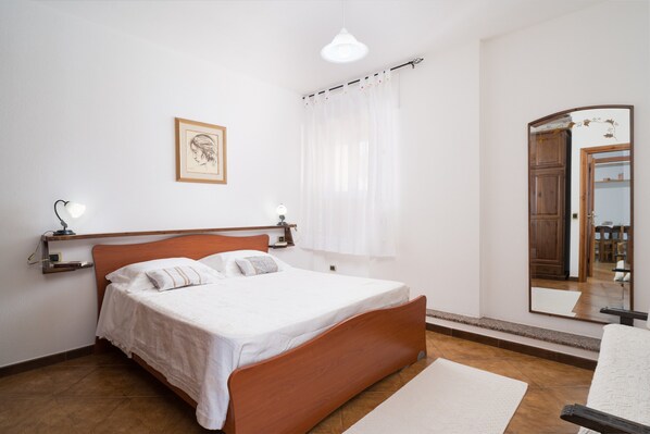 Une chambre à coucher avec un lit en bois, une table de chevet avec une lampe, un tableau encadré au mur et un miroir qui reflète une porte et une armoire.