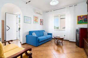 A living room with a blue sofa, a yellow armchair, a small table, and a kitchen area with a red appliance.