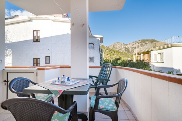 A balcony with a table and chairs, a view of buildings, and a mountain in the background.