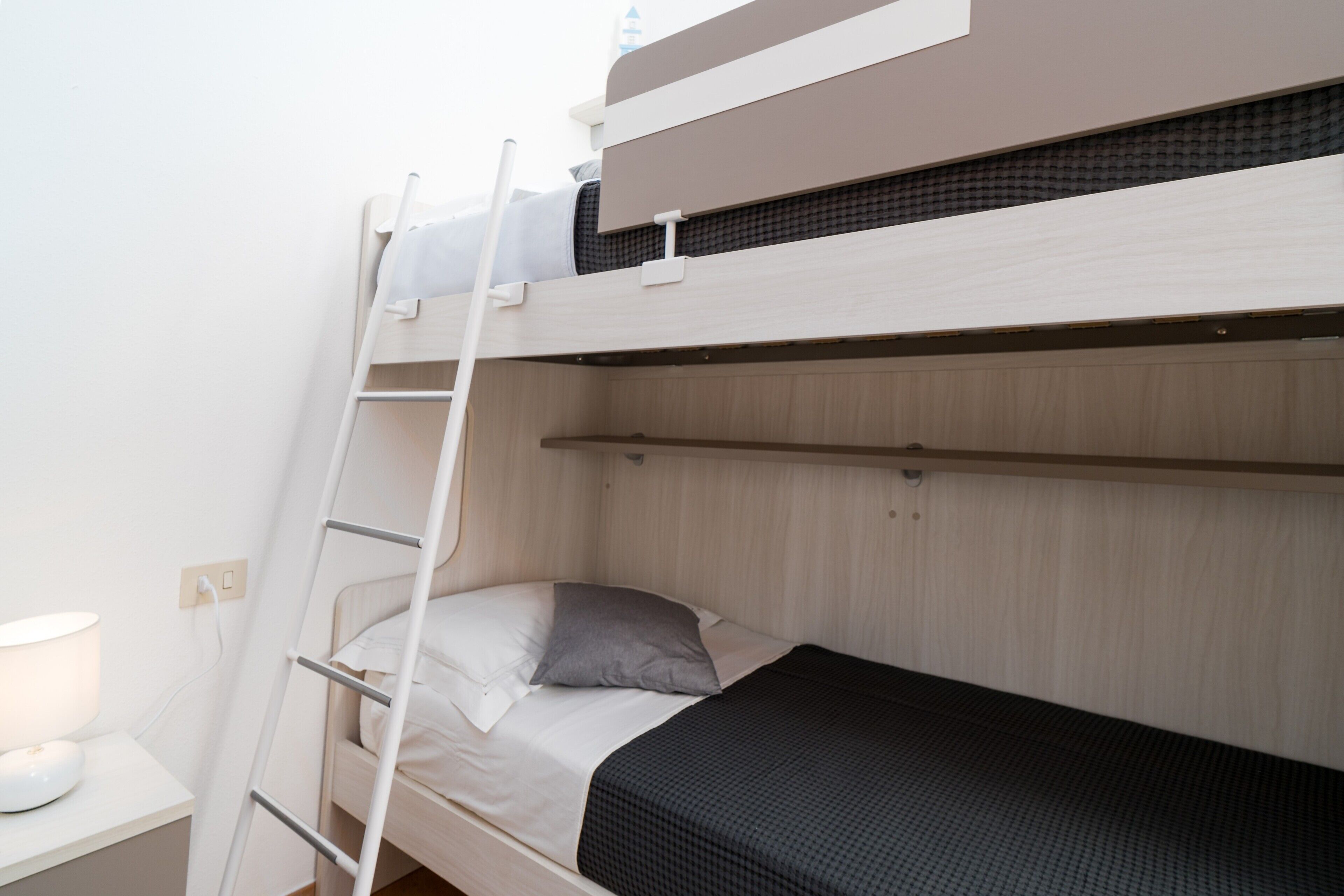 Un letto a castello con una scala, un comodino con una lampada e una mensola a parete.