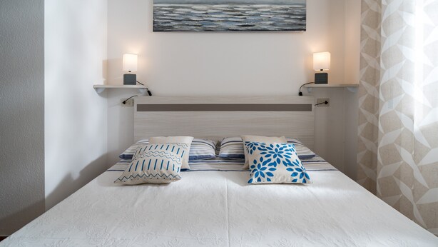 Une chambre à coucher avec un lit, des oreillers, une table de chevet, un tableau accroché au mur et un rideau.