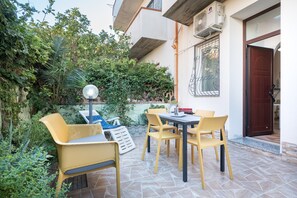 Une terrasse extérieure avec une table et des chaises, entourée de verdure et donnant sur un bâtiment doté d’un balcon.