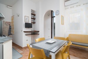 Un espace repas comprenant une table, des chaises, un banc, un téléviseur et un coin cuisine avec une cuisinière.