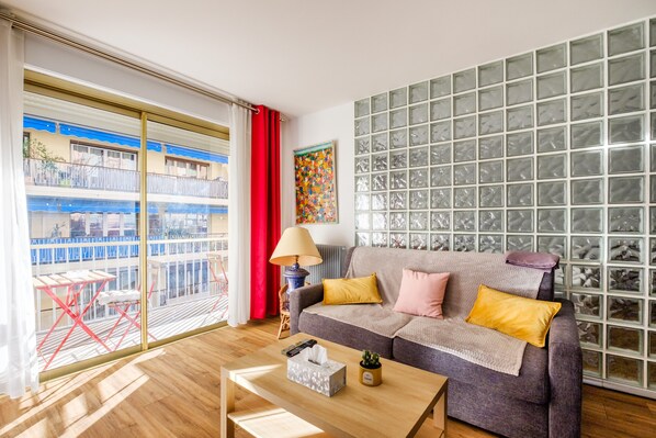 A living room with a sofa, a coffee table, a lamp, and a view of a balcony.
