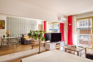 A modern living room with a TV, sofa, dining table, chairs, and a balcony with red curtains. - Luxury apartment in Cannes – Ideal for a relaxing getaway (Cannes)