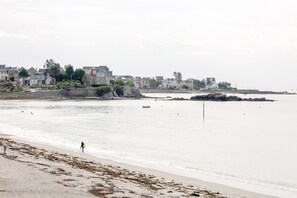 Une plage côtière avec des maisons en arrière-plan, un rivage sablonneux et une eau calme.