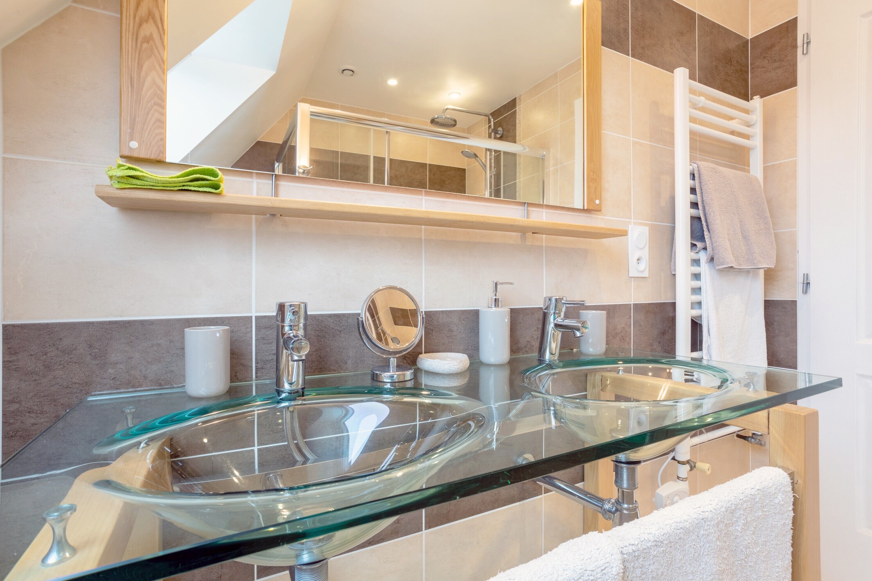 A modern bathroom with two glass sinks, a mirror, and a towel rack.