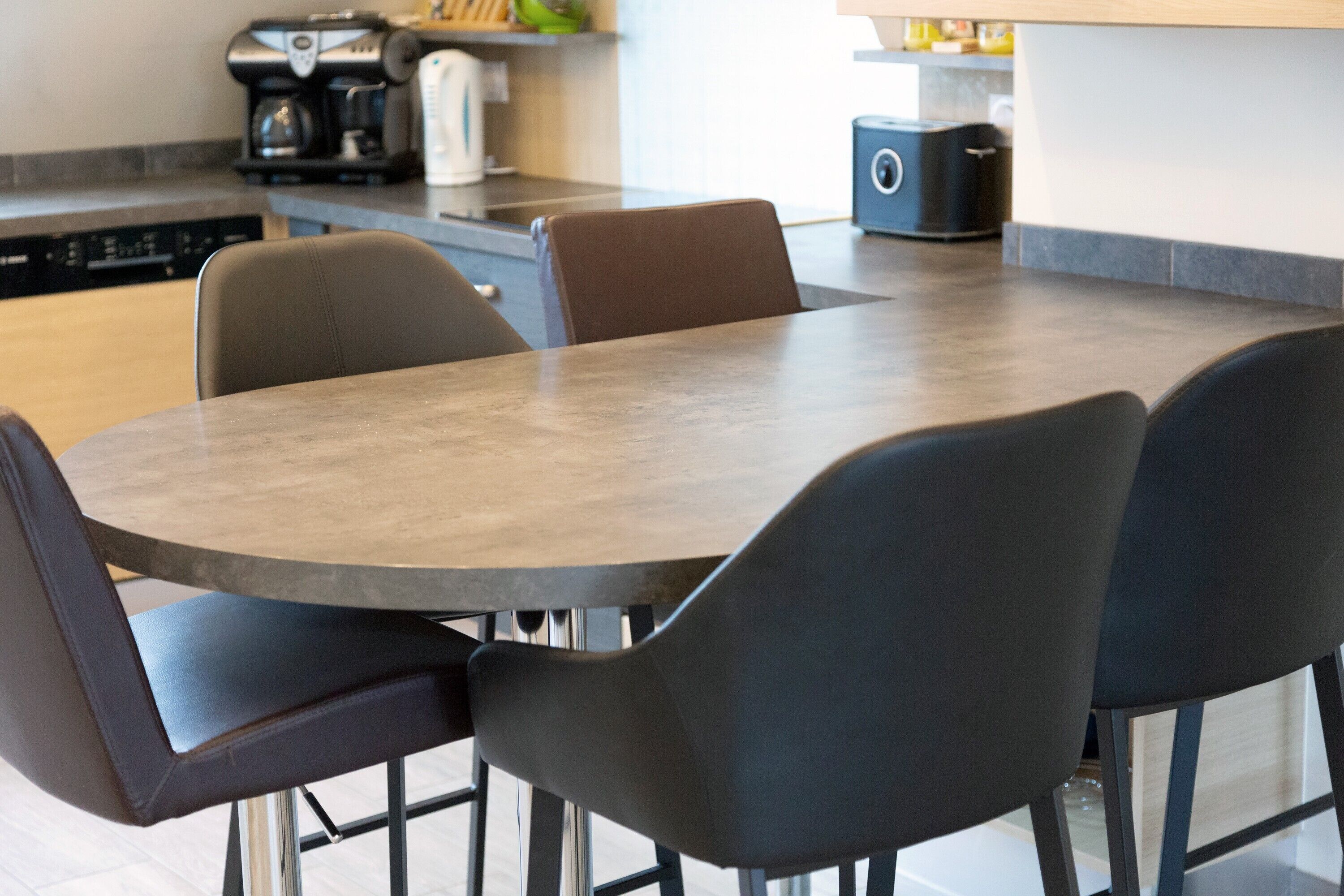 Une cuisine moderne avec une table de salle à manger ronde, des chaises noires et une machine à café.