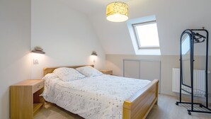 Een slaapkamer met een bed, nachtkastjes, een hanglamp, een radiator en een raam.