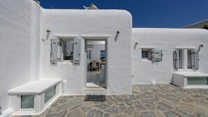 A white-walled building with a stone-paved courtyard, a door leading to an interior space, and a small bench. - Villa "Harmony' with Sea View, Private Pool & Wi-Fi (Mykonos)